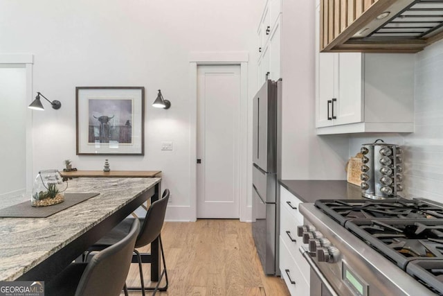 kitchen with light wood-type flooring, appliances with stainless steel finishes, under cabinet range hood, white cabinetry, and tasteful backsplash