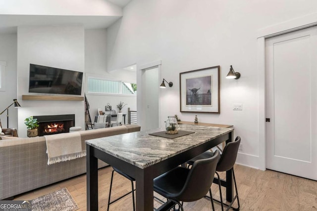 dining room featuring light wood-style flooring, a warm lit fireplace, and a towering ceiling