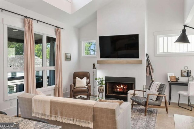 living area with vaulted ceiling, wood finished floors, baseboards, and a warm lit fireplace