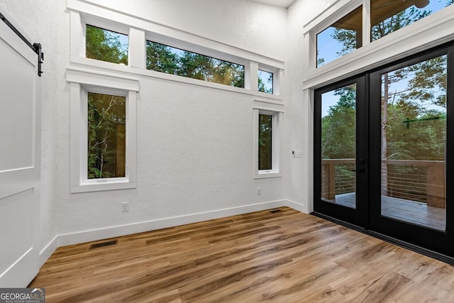 empty room with french doors, a high ceiling, a barn door, and light hardwood / wood-style floors