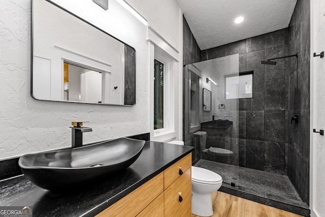 bathroom featuring toilet, hardwood / wood-style floors, vanity, a textured ceiling, and a tile shower