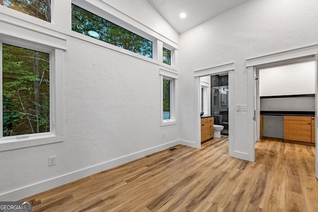 unfurnished bedroom featuring light wood-type flooring, high vaulted ceiling, and ensuite bath