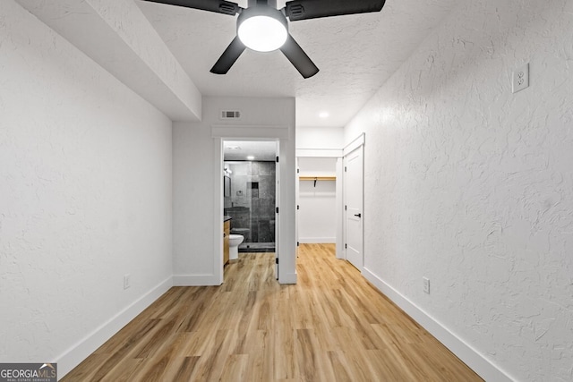 interior space with a textured ceiling, ceiling fan, light wood-type flooring, and ensuite bathroom