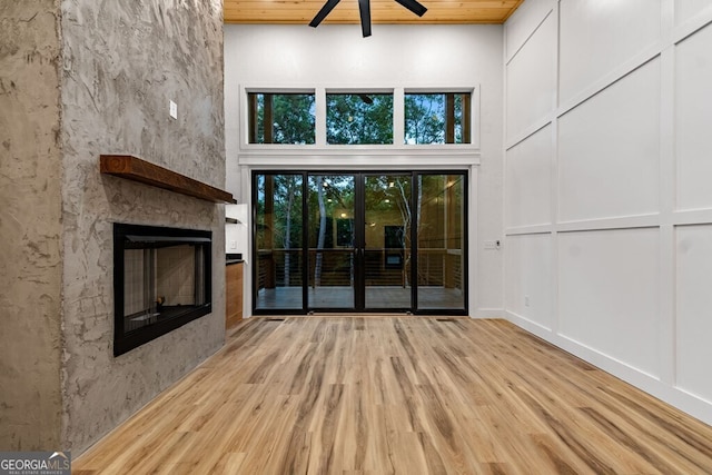 unfurnished living room with wooden ceiling, light hardwood / wood-style floors, a large fireplace, ceiling fan, and a high ceiling