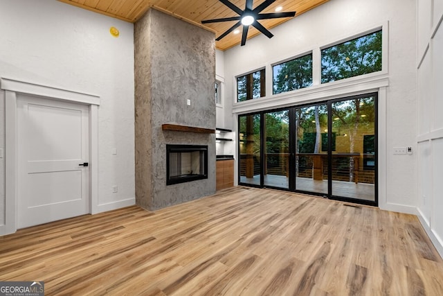 unfurnished living room featuring a high ceiling, wooden ceiling, wood-type flooring, a large fireplace, and ceiling fan