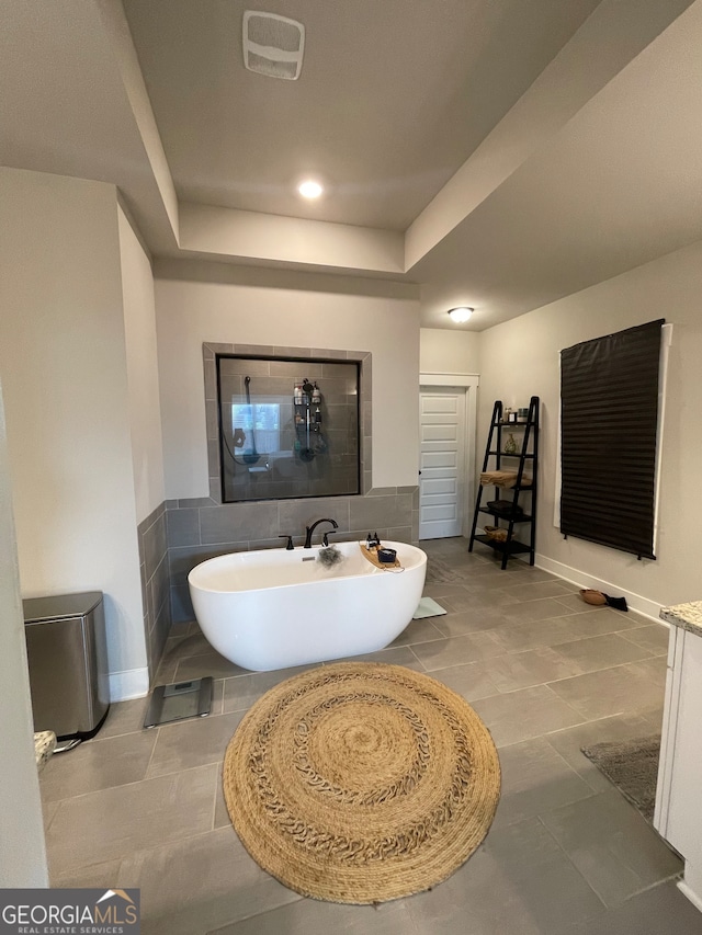 bathroom with tile patterned floors, a tray ceiling, a tub to relax in, and vanity