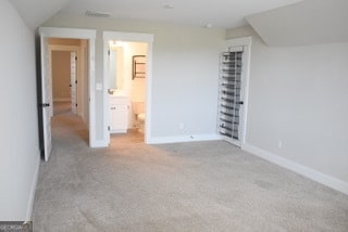 unfurnished bedroom featuring lofted ceiling, light carpet, and ensuite bath