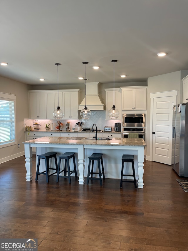 kitchen with an island with sink, dark hardwood / wood-style floors, light stone countertops, and premium range hood