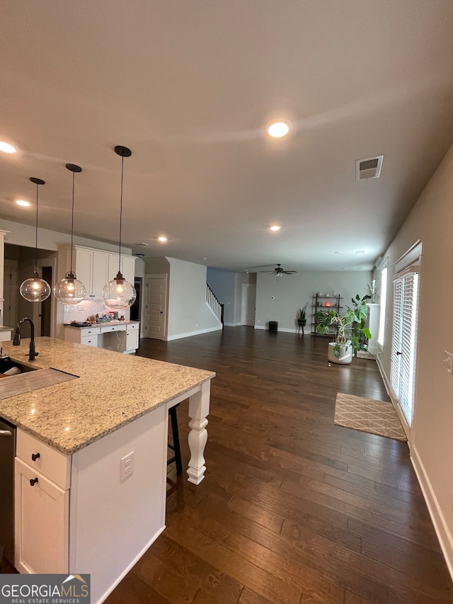 kitchen with dark wood-type flooring, hanging light fixtures, a kitchen breakfast bar, and a center island with sink