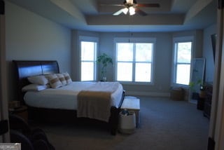 carpeted bedroom with a raised ceiling and ceiling fan