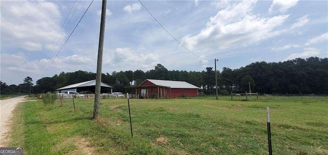 view of yard featuring driveway, a rural view, fence, and a wooded view