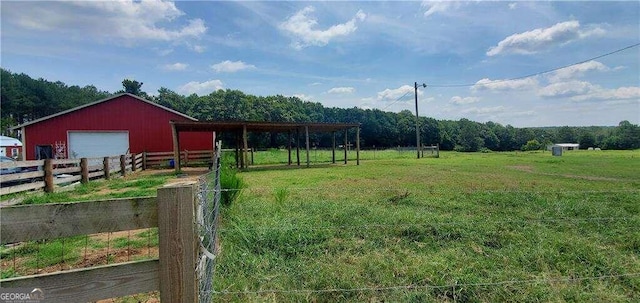 view of yard featuring an outbuilding, fence, a garage, a rural view, and an outdoor structure