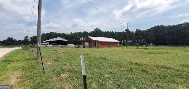 view of yard with an outbuilding, a rural view, an outdoor structure, fence, and driveway