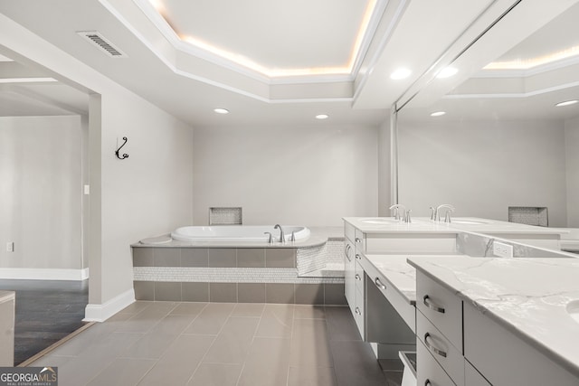 bathroom with tile patterned flooring, a tray ceiling, tiled tub, and vanity