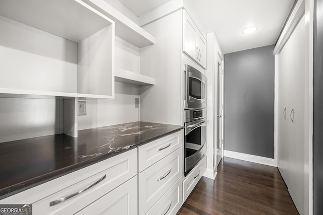 kitchen featuring dark stone counters, appliances with stainless steel finishes, dark hardwood / wood-style flooring, and white cabinets