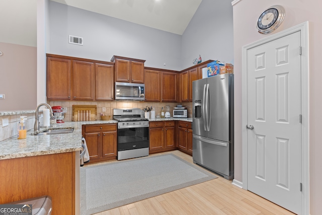 kitchen featuring tasteful backsplash, sink, high vaulted ceiling, stainless steel appliances, and light hardwood / wood-style flooring