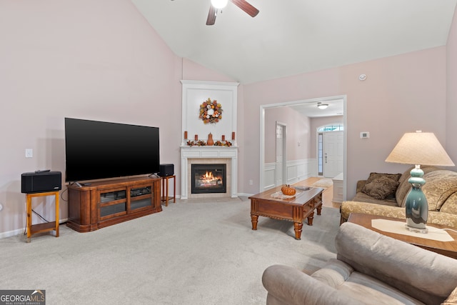 living room with ceiling fan, a tiled fireplace, vaulted ceiling, and light carpet