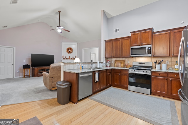 kitchen with light stone counters, tasteful backsplash, high vaulted ceiling, stainless steel appliances, and light hardwood / wood-style flooring