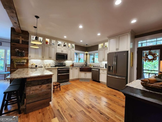 kitchen with light hardwood / wood-style flooring, hanging light fixtures, appliances with stainless steel finishes, and tasteful backsplash