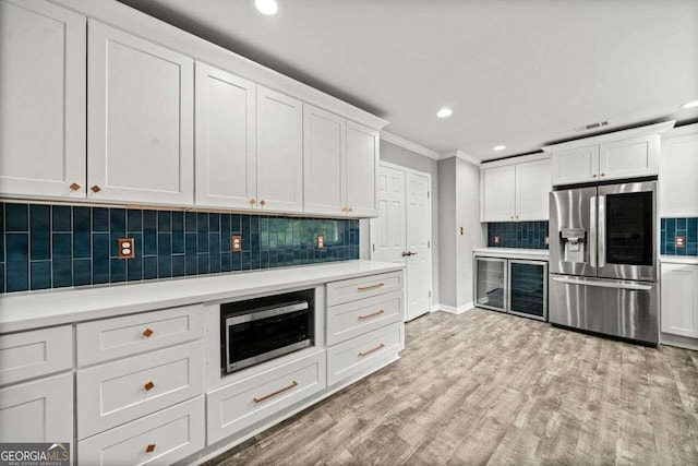 kitchen with white cabinets, crown molding, appliances with stainless steel finishes, light hardwood / wood-style floors, and tasteful backsplash