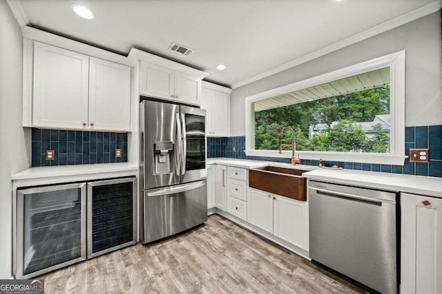 kitchen with crown molding, tasteful backsplash, appliances with stainless steel finishes, white cabinets, and light hardwood / wood-style floors