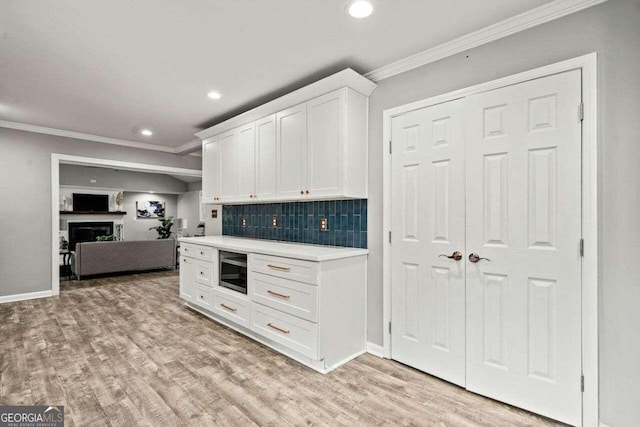 kitchen with backsplash, white cabinets, ornamental molding, light wood-type flooring, and stainless steel microwave