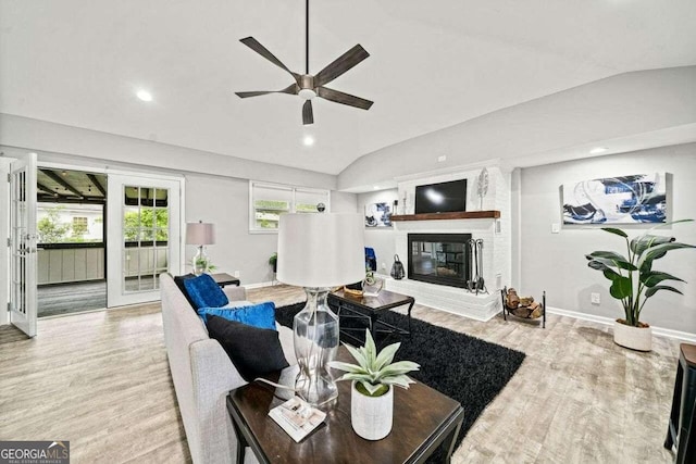 living room with light wood-type flooring, vaulted ceiling, a fireplace, and ceiling fan