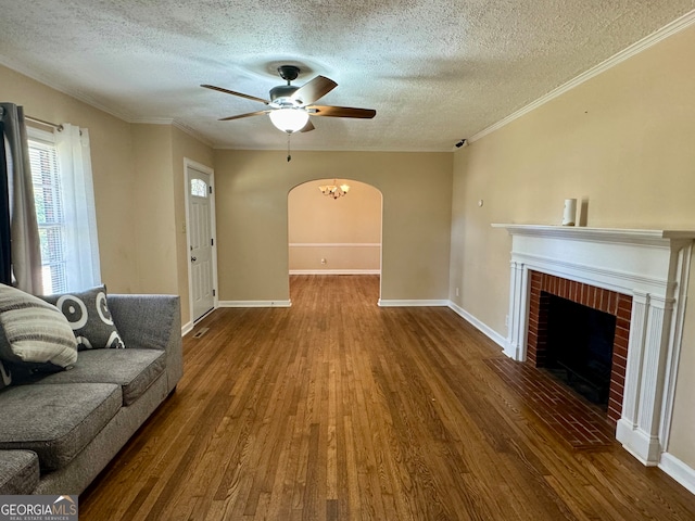 unfurnished living room featuring a textured ceiling, wood-type flooring, ornamental molding, a brick fireplace, and ceiling fan