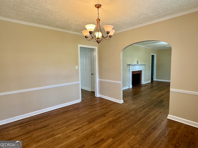 empty room featuring dark wood-type flooring, crown molding, a notable chandelier, and a brick fireplace