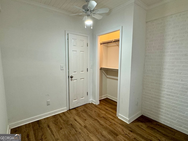 unfurnished bedroom featuring crown molding, dark hardwood / wood-style flooring, brick wall, a closet, and ceiling fan