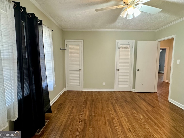 unfurnished bedroom featuring two closets, crown molding, hardwood / wood-style floors, ceiling fan, and a textured ceiling