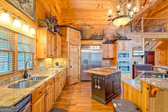 kitchen featuring sink, light hardwood / wood-style flooring, wooden walls, built in appliances, and light stone counters