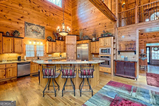 kitchen with light hardwood / wood-style flooring, hanging light fixtures, wooden walls, a center island, and built in appliances