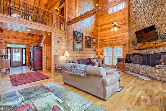 living room featuring ceiling fan, wooden walls, a stone fireplace, and light hardwood / wood-style flooring