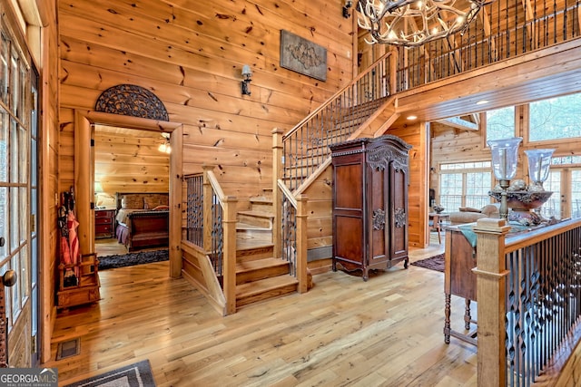 stairway featuring an inviting chandelier, a towering ceiling, wooden walls, and wood-type flooring