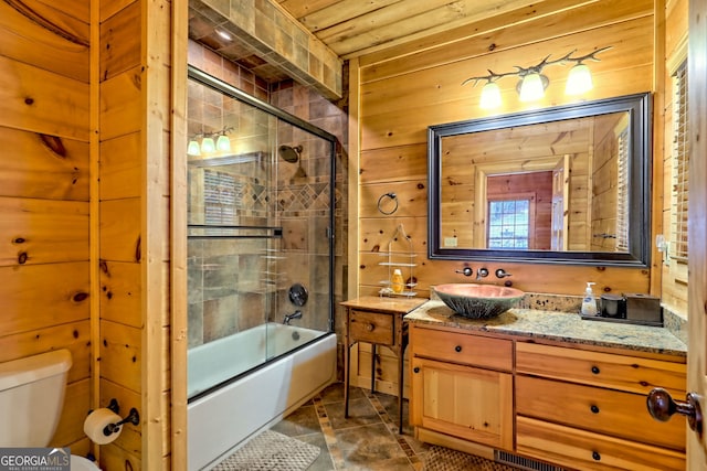 full bathroom with vanity, toilet, combined bath / shower with glass door, and wood walls