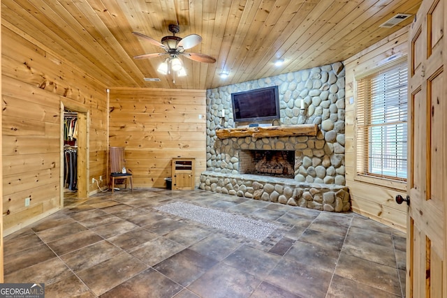 unfurnished living room featuring ceiling fan, a stone fireplace, wood ceiling, and wood walls