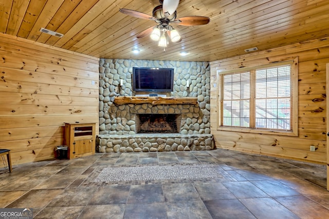 unfurnished living room with wood walls, a stone fireplace, and wooden ceiling