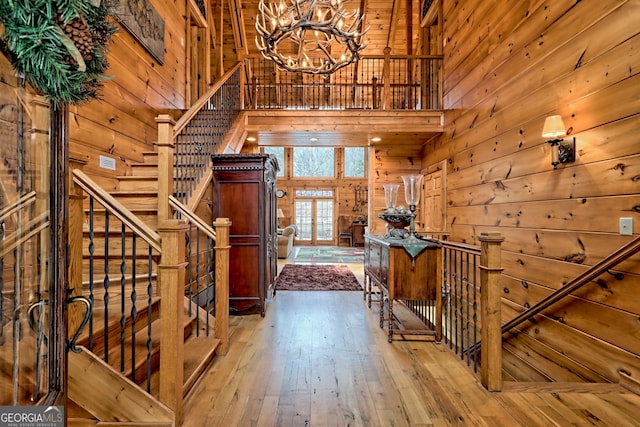 foyer entrance featuring hardwood / wood-style floors, a notable chandelier, wooden walls, and a high ceiling