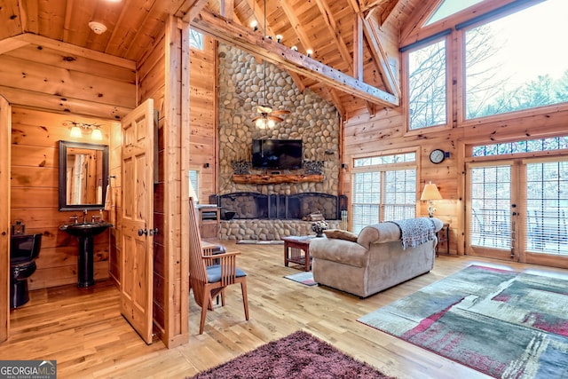 living room featuring wooden walls, light wood-type flooring, a stone fireplace, and wooden ceiling