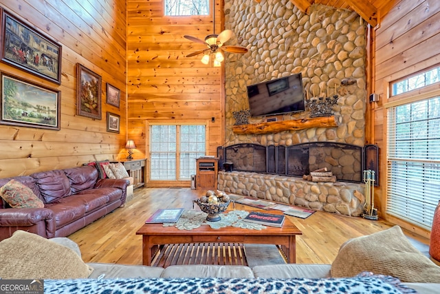 living room with hardwood / wood-style floors, beam ceiling, wooden walls, high vaulted ceiling, and a stone fireplace