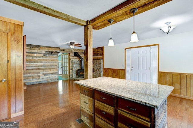 kitchen featuring decorative light fixtures, a wood stove, light hardwood / wood-style flooring, ceiling fan, and wooden walls