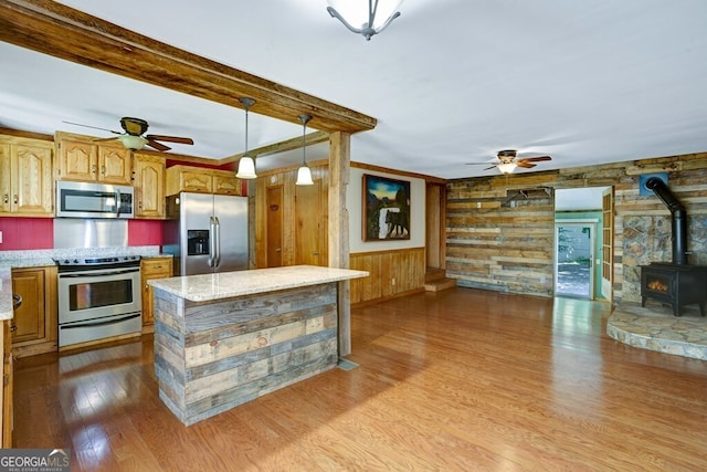 kitchen featuring a wood stove, wooden walls, appliances with stainless steel finishes, and light hardwood / wood-style floors