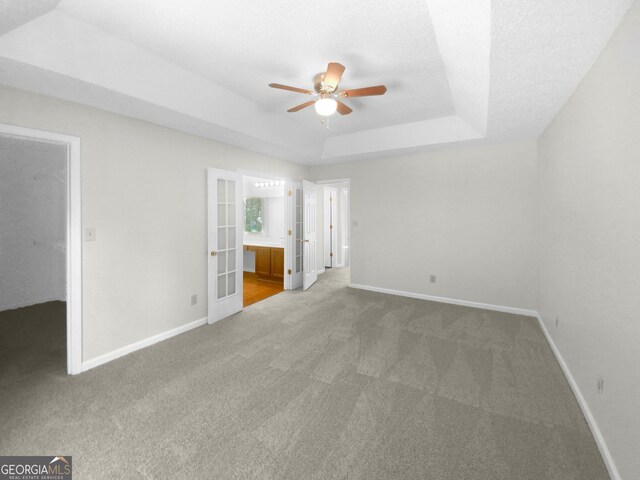 unfurnished bedroom featuring a tray ceiling, ceiling fan, carpet, and ensuite bath