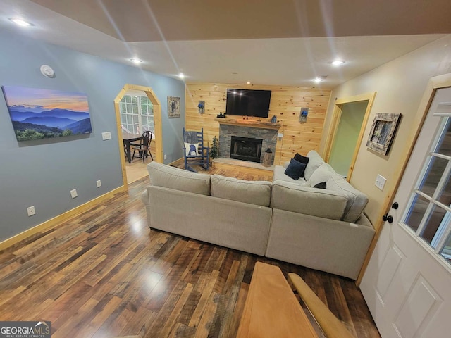 living room featuring wood walls, a stone fireplace, and wood-type flooring