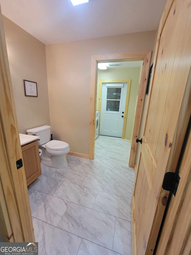 bathroom featuring tile patterned flooring, toilet, washing machine and clothes dryer, and vanity