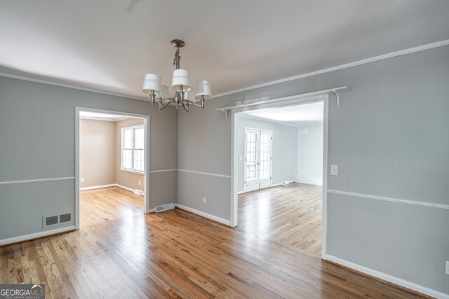 empty room with hardwood / wood-style floors, crown molding, and a notable chandelier