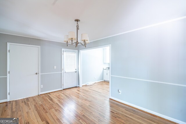 unfurnished dining area featuring ornamental molding, light wood-type flooring, and a chandelier