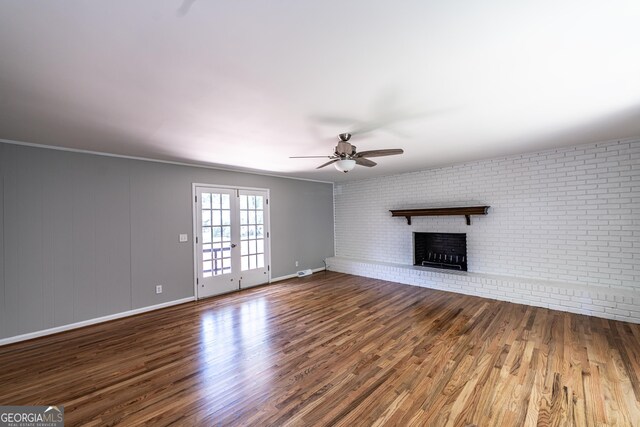 unfurnished living room featuring brick wall, a fireplace, french doors, hardwood / wood-style flooring, and ceiling fan