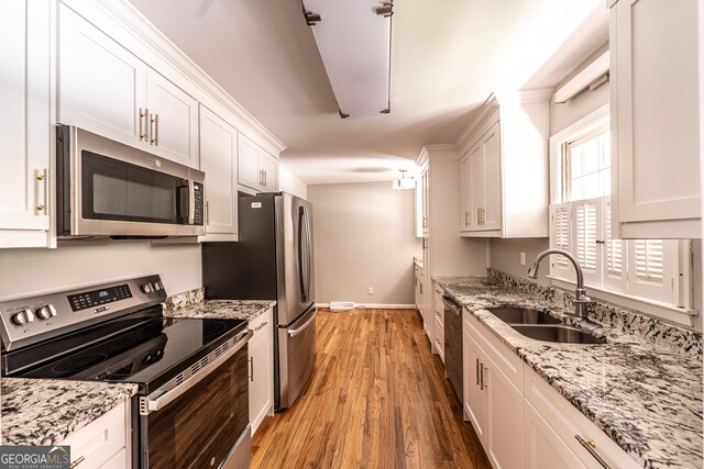 kitchen featuring white cabinets, light stone counters, stainless steel appliances, sink, and wood-type flooring